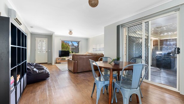 A modern living room with a sofa, a dining table with chairs, a TV, and a sliding glass door leading to an outdoor area. - Serenity Now Inverloch (Inverloch)