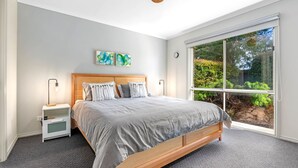 A bedroom with a large window, a wooden bed, a nightstand, and two abstract paintings on the wall. - Serenity Now Inverloch (Inverloch)
