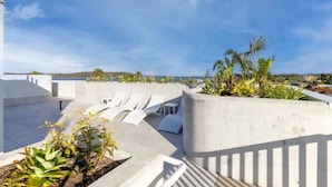 A rooftop terrace with white lounge chairs, concrete planters with tropical plants, and a view of the sea. - Elegant 2-Bed Apartment with Stunning Views (Batemans Bay)