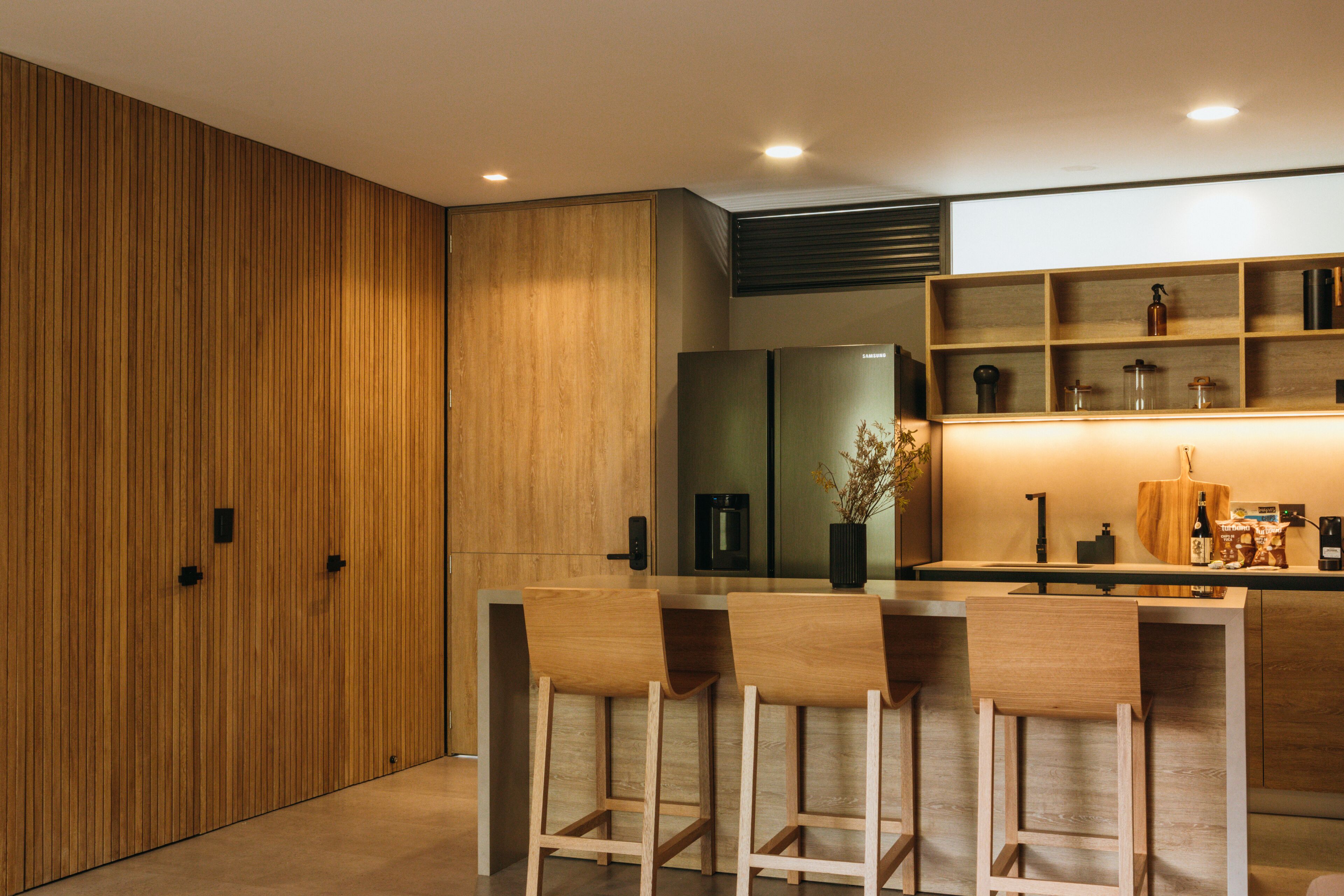 A modern kitchen with wooden cabinets, a central island with bar stools, and built-in appliances.