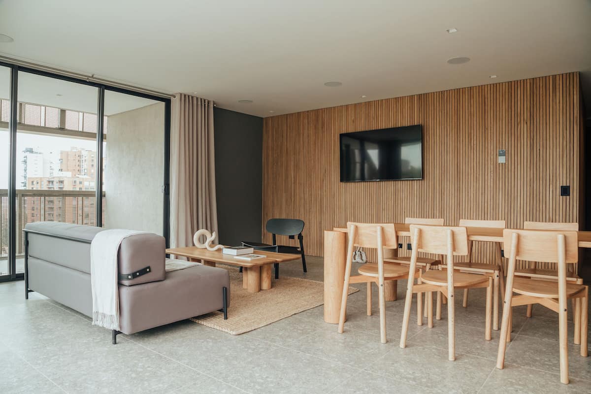 A modern living room with a sofa, coffee table, and dining area with wooden chairs and a TV mounted on the wall.