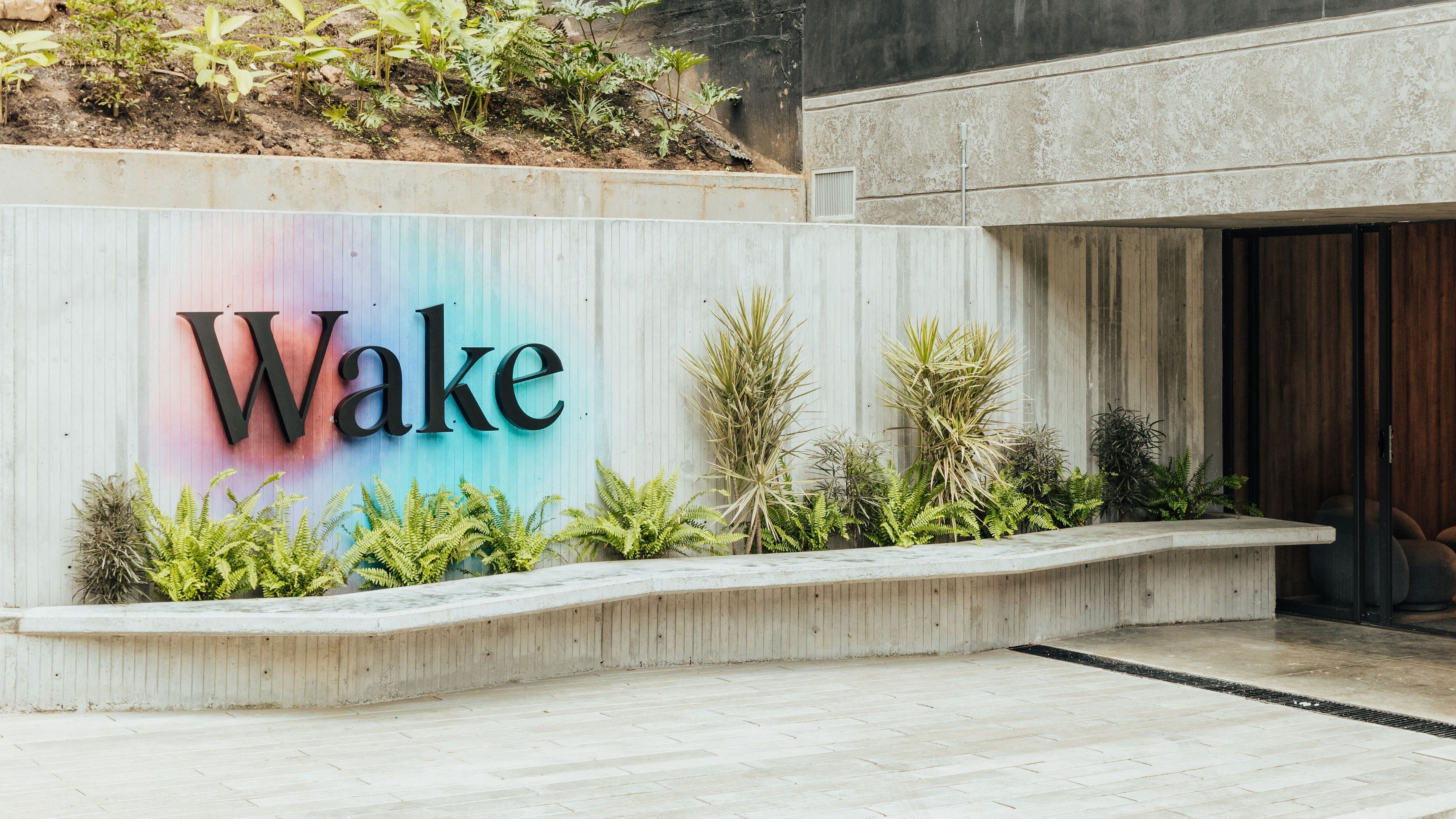 A sign with the word "Wake" in large letters, surrounded by greenery and a concrete structure.