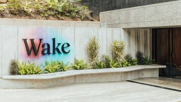 Un cartel con la palabra 'Wake' en letras grandes, rodeado de follaje y una estructura de concreto.
