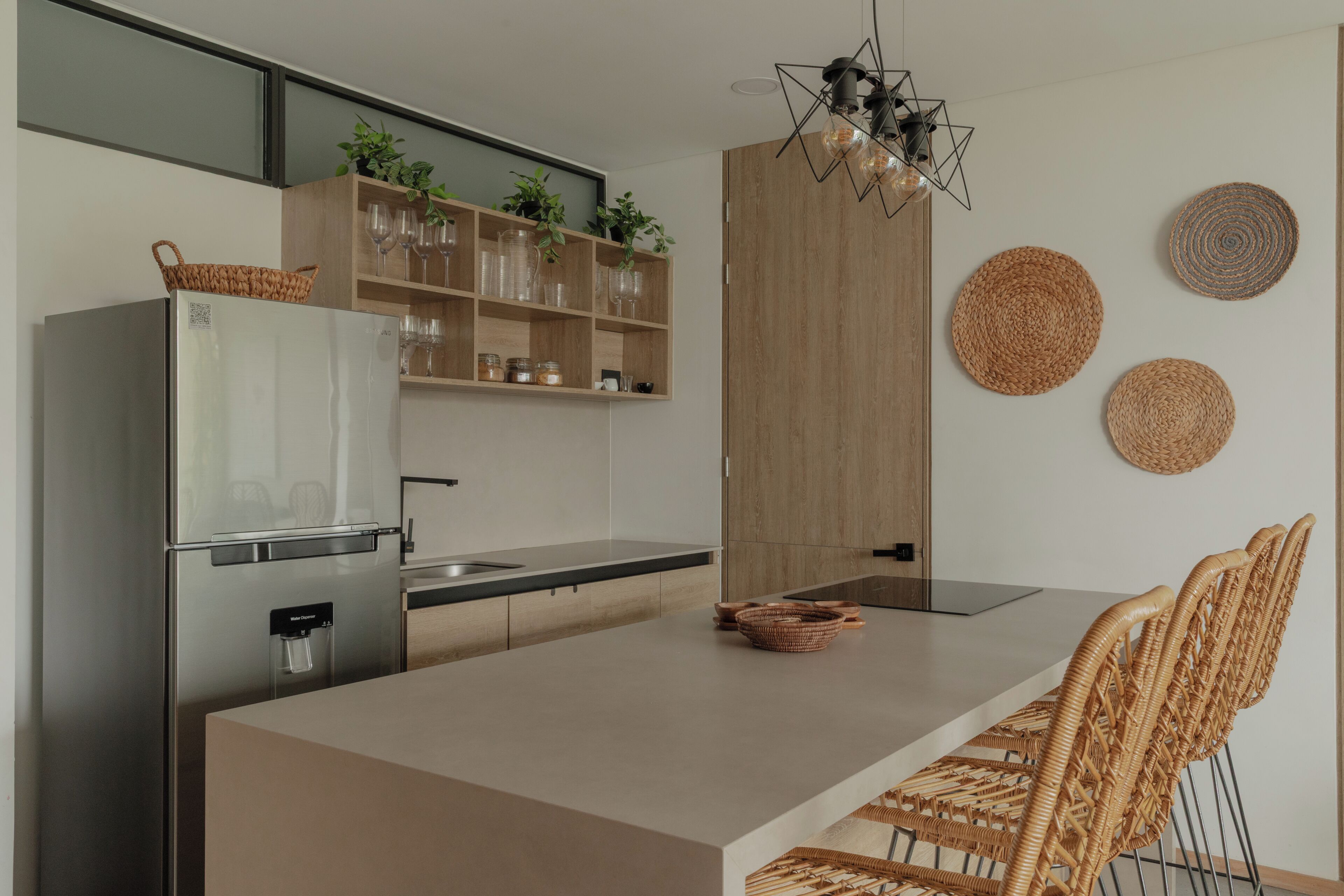 A modern kitchen with a built-in refrigerator, wooden cabinets, a central island, and wicker chairs.