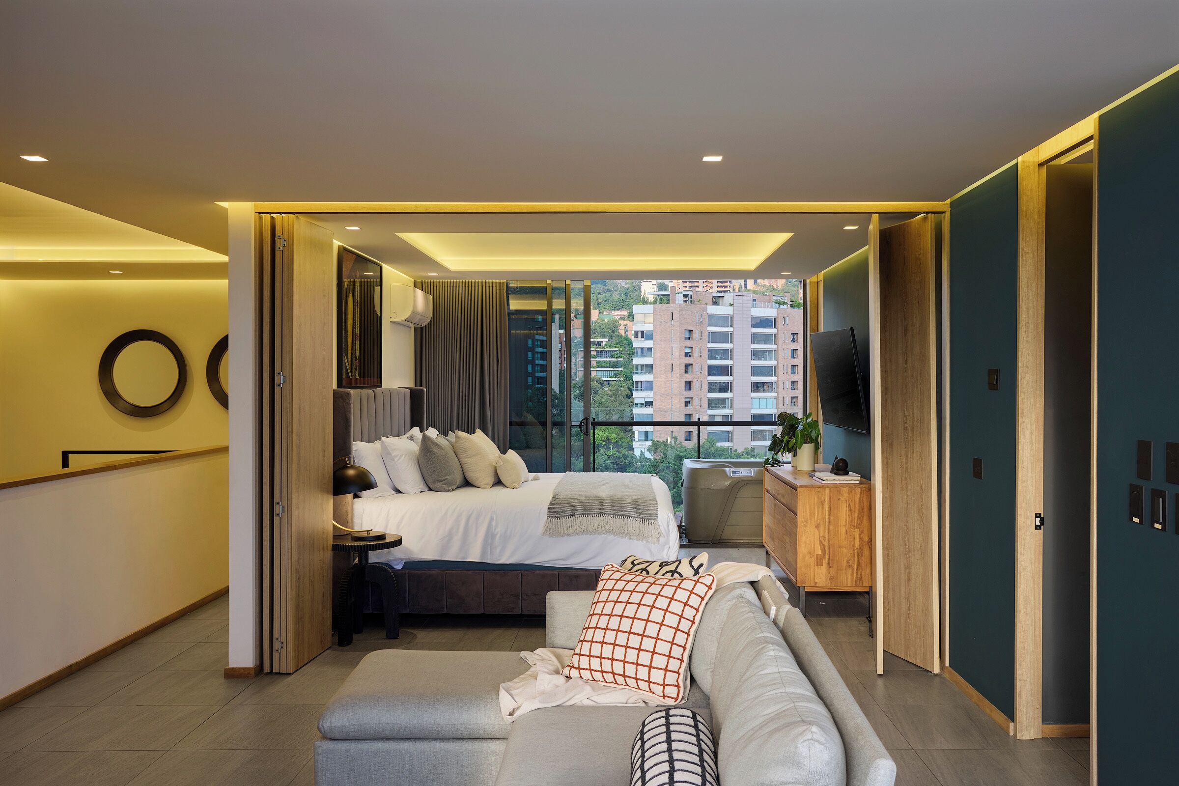 A modern hotel room with a bed, a sofa, a desk, and a TV.