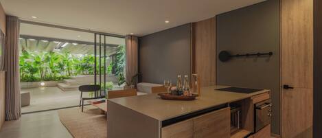 A modern kitchen with a central island, wooden cabinets, and a view of a green garden through large windows.