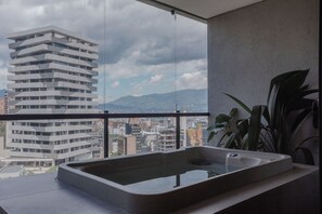 A modern bathroom with a large window, a bathtub, and a view of a cityscape. - Wake Living (Medellín)