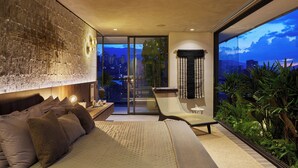 Un dormitorio moderno con una cama grande, un sillón de descanso y vistas a la ciudad a través de amplios ventanales.