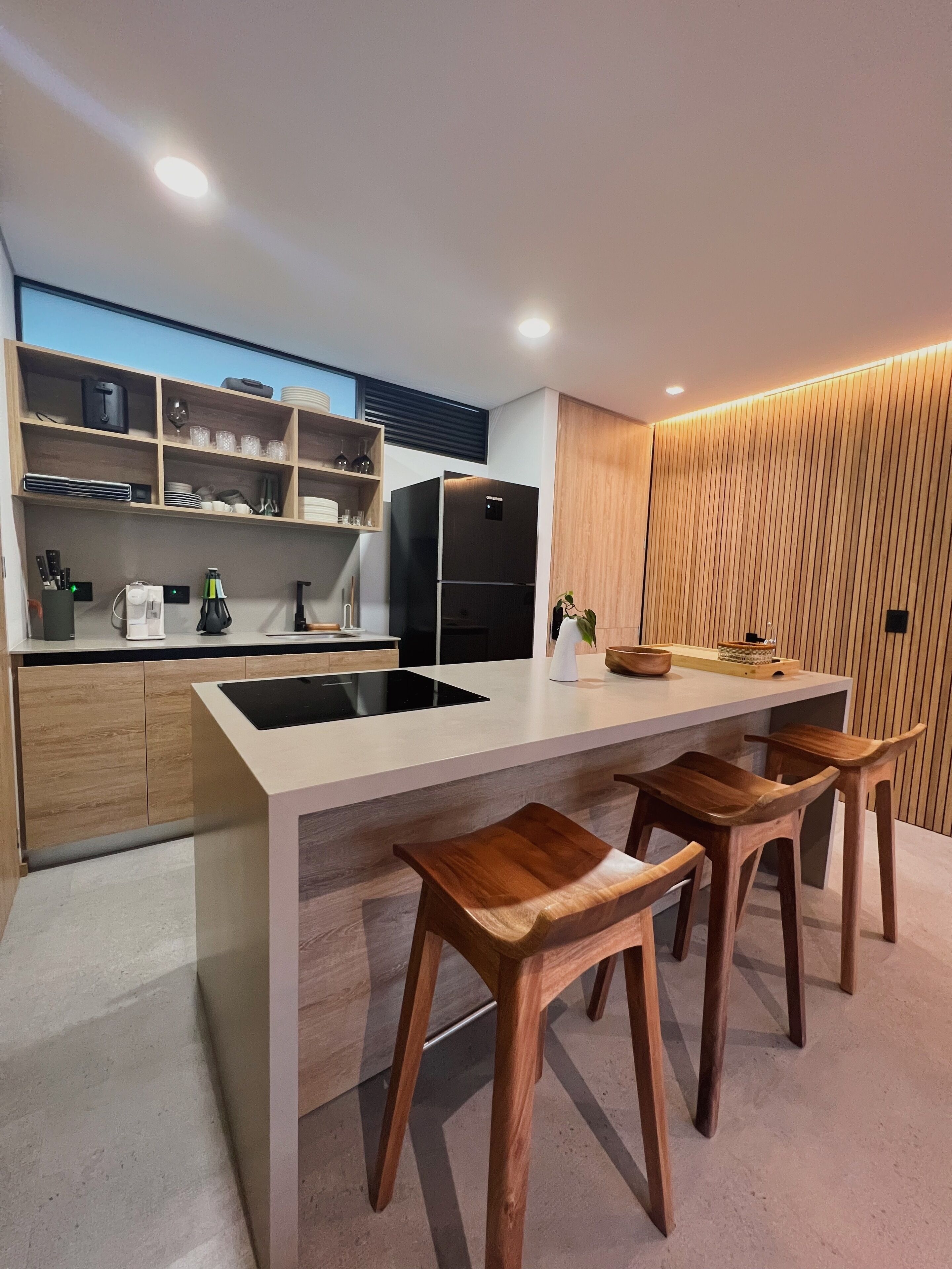 A modern kitchen with a central island, wooden bar stools, and built-in appliances.
