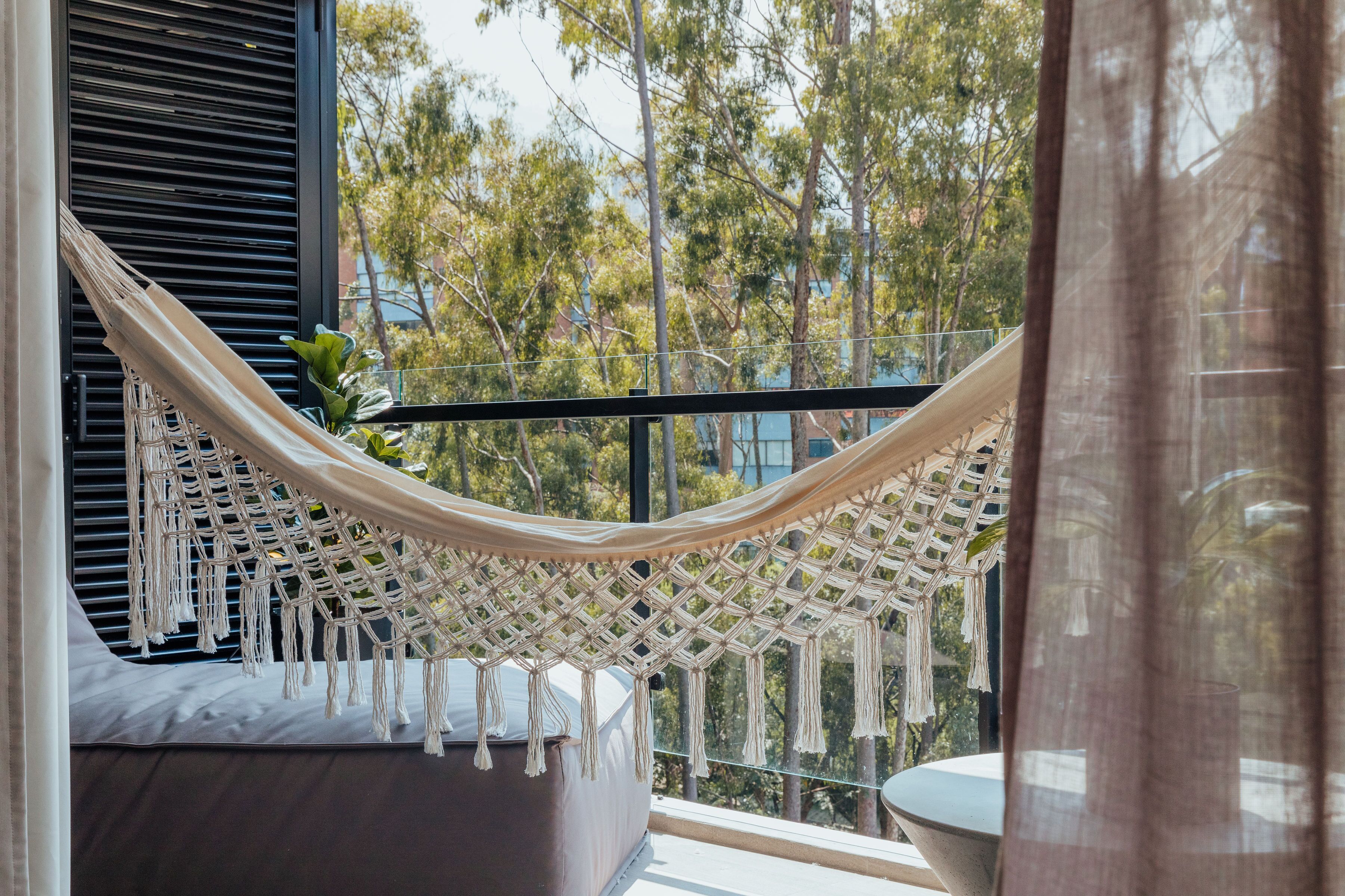 Un hamac sur un balcon, avec vue sur les arbres et les immeubles.