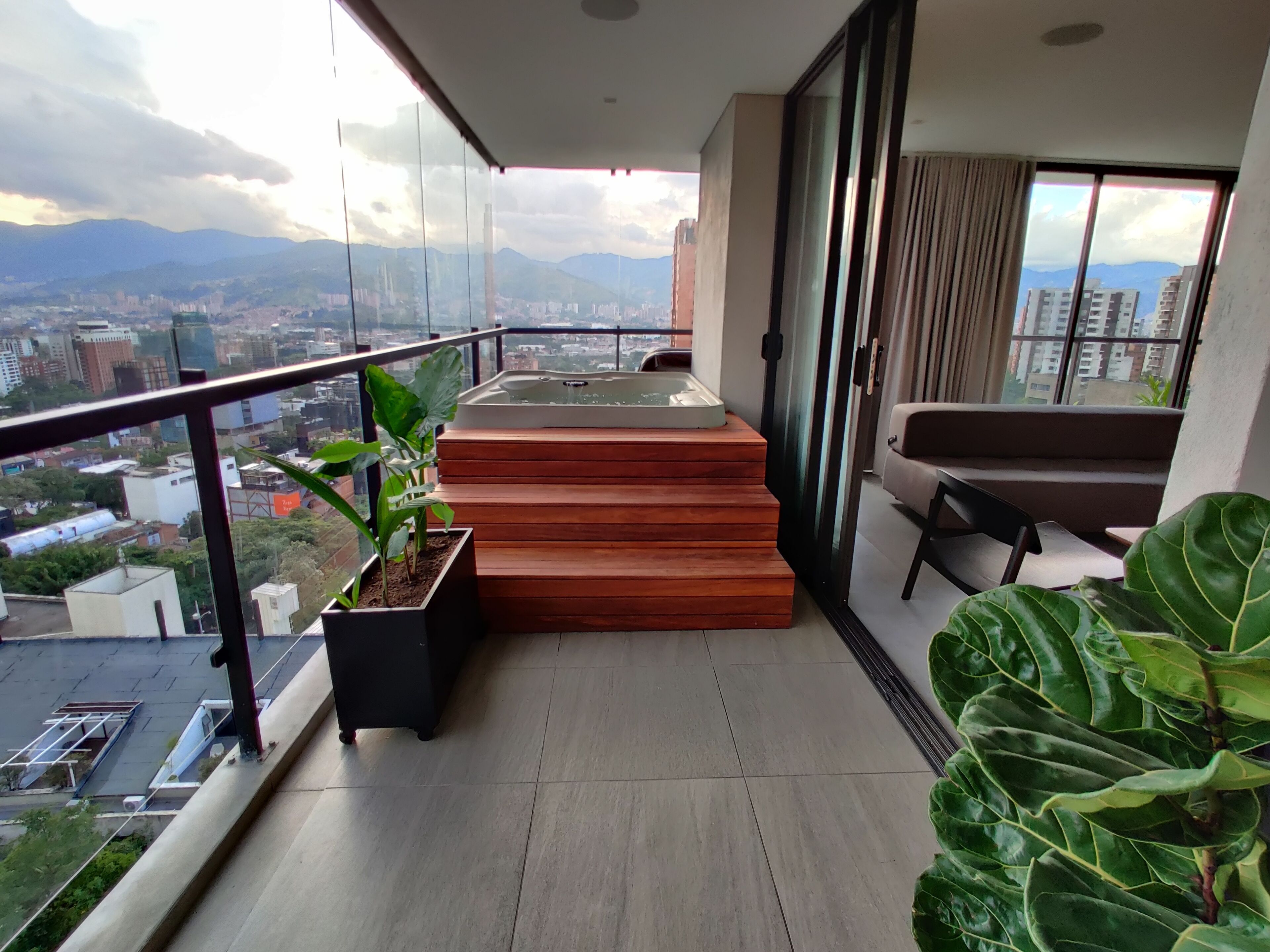 A balcony with a hot tub, wooden steps, a sofa, and potted plants.