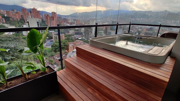 Un balcón con hidromasaje, escalones de madera y una planta en maceta.