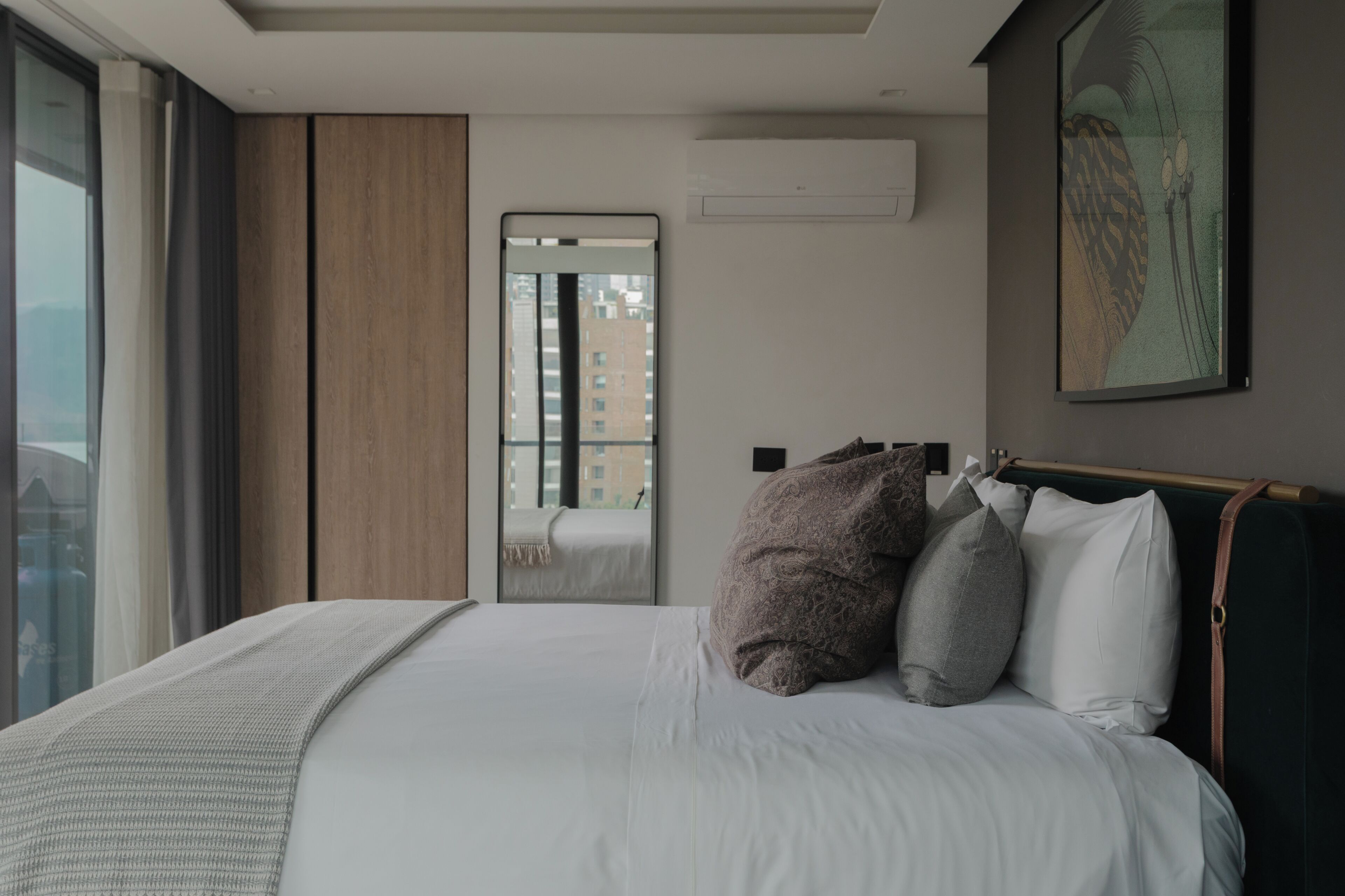A modern hotel room with a large bed, a view of the city through a window, and a painting on the wall.
