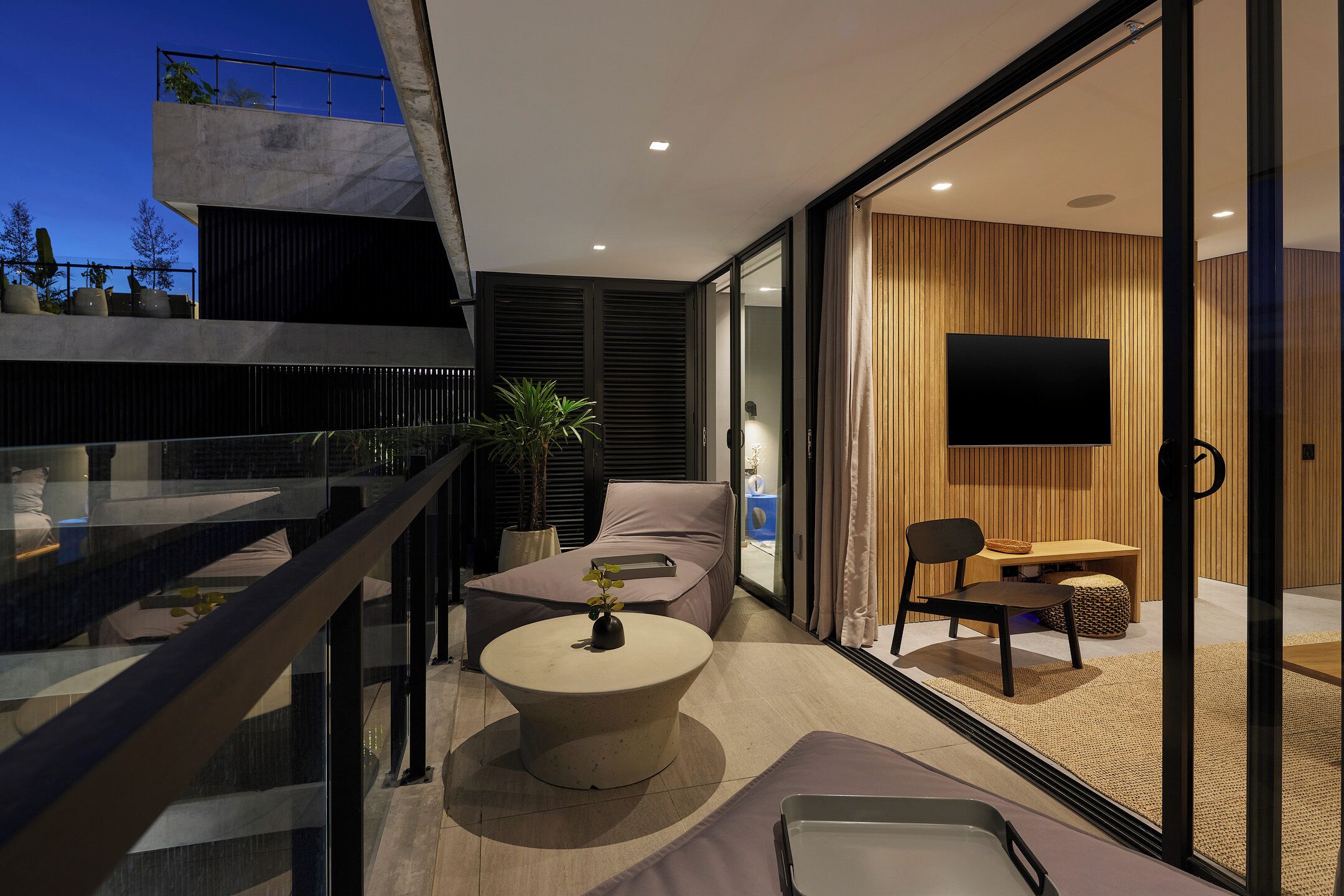 A modern living room with a glass door leading to a balcony, a round coffee table, and a flat-screen TV mounted on the wall.