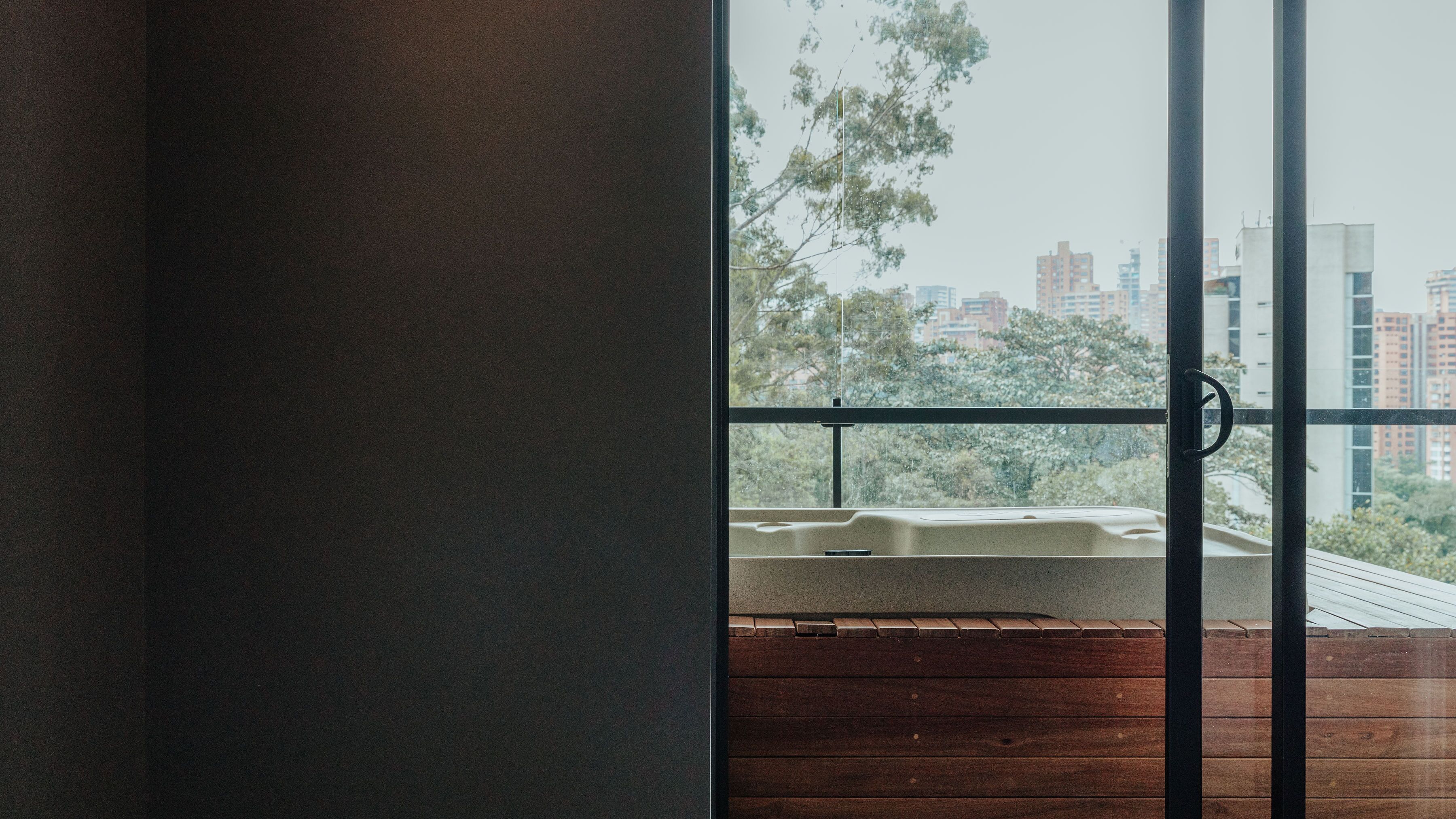 A view from a balcony with a wooden floor and a metal railing, overlooking a cityscape with buildings and trees.