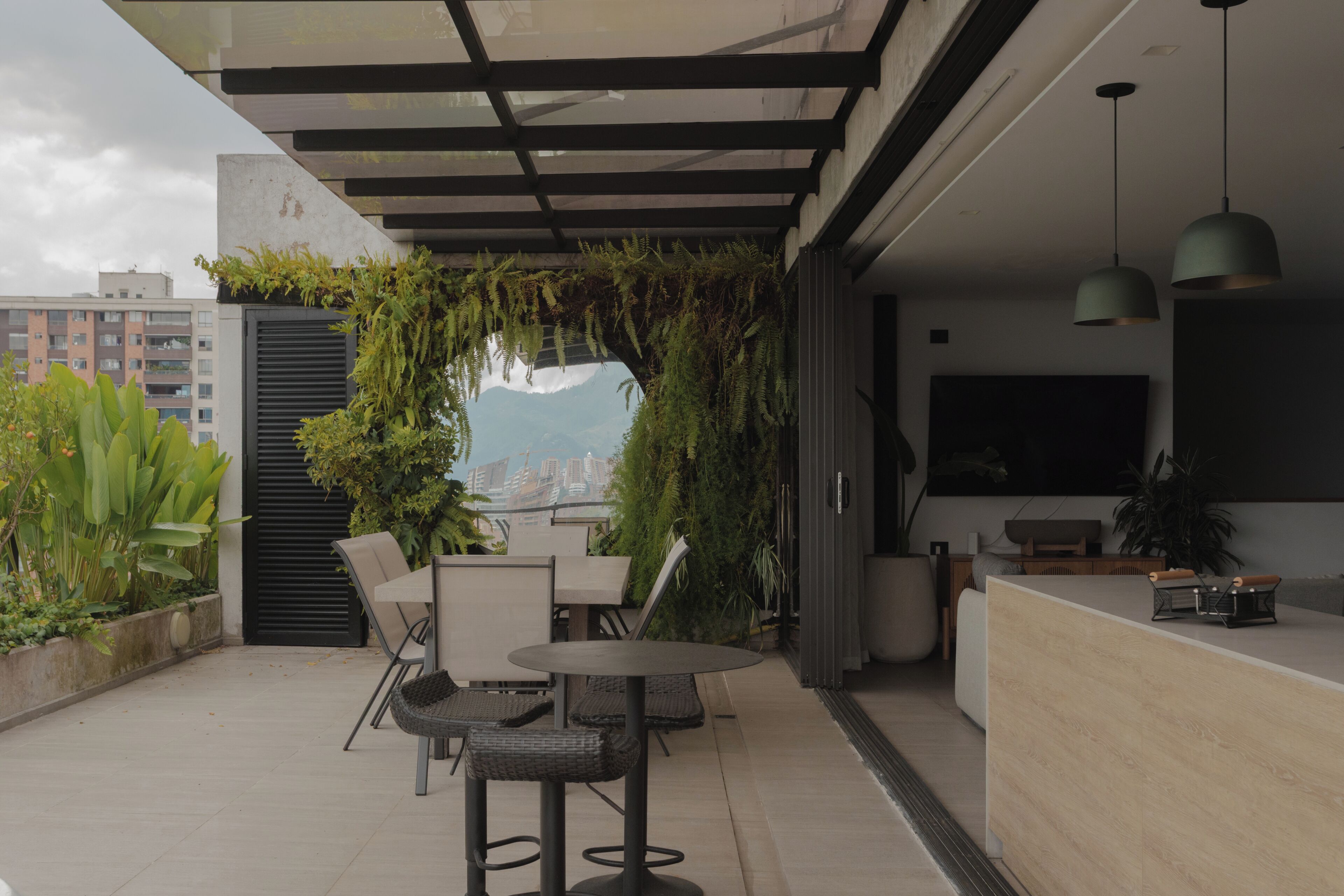 Een moderne zithoek buiten met uitzicht op een stadsgezicht, met een ronde tafel, stoelen en plantenpotten.
