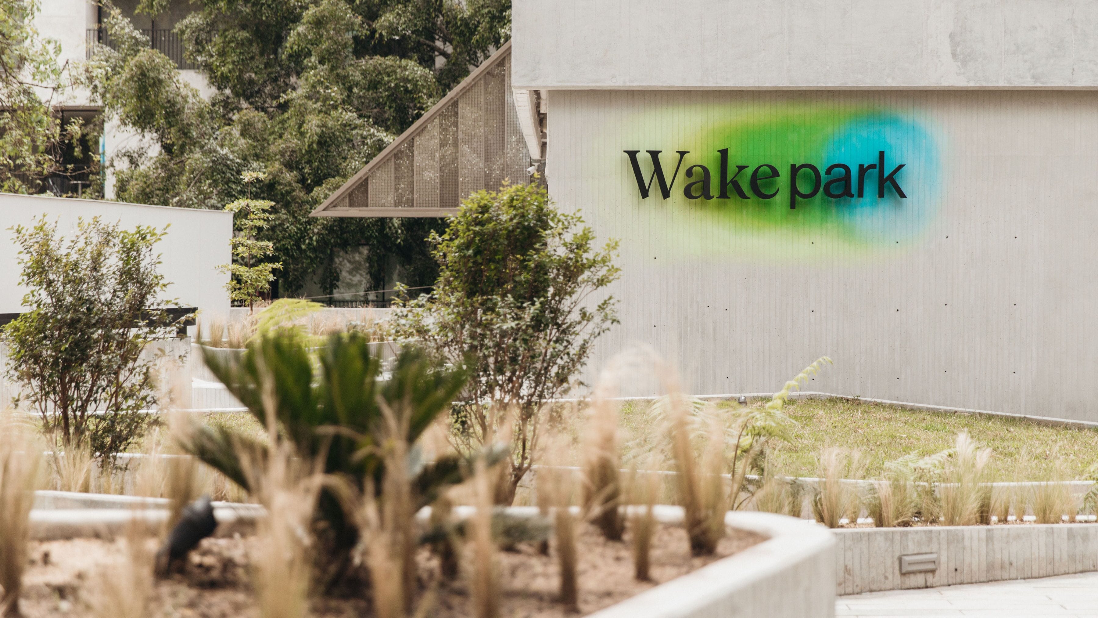 Un bâtiment sur lequel est apposée une enseigne indiquant « Wakepark », ainsi qu’un espace aménagé avec différentes espèces de plantes.