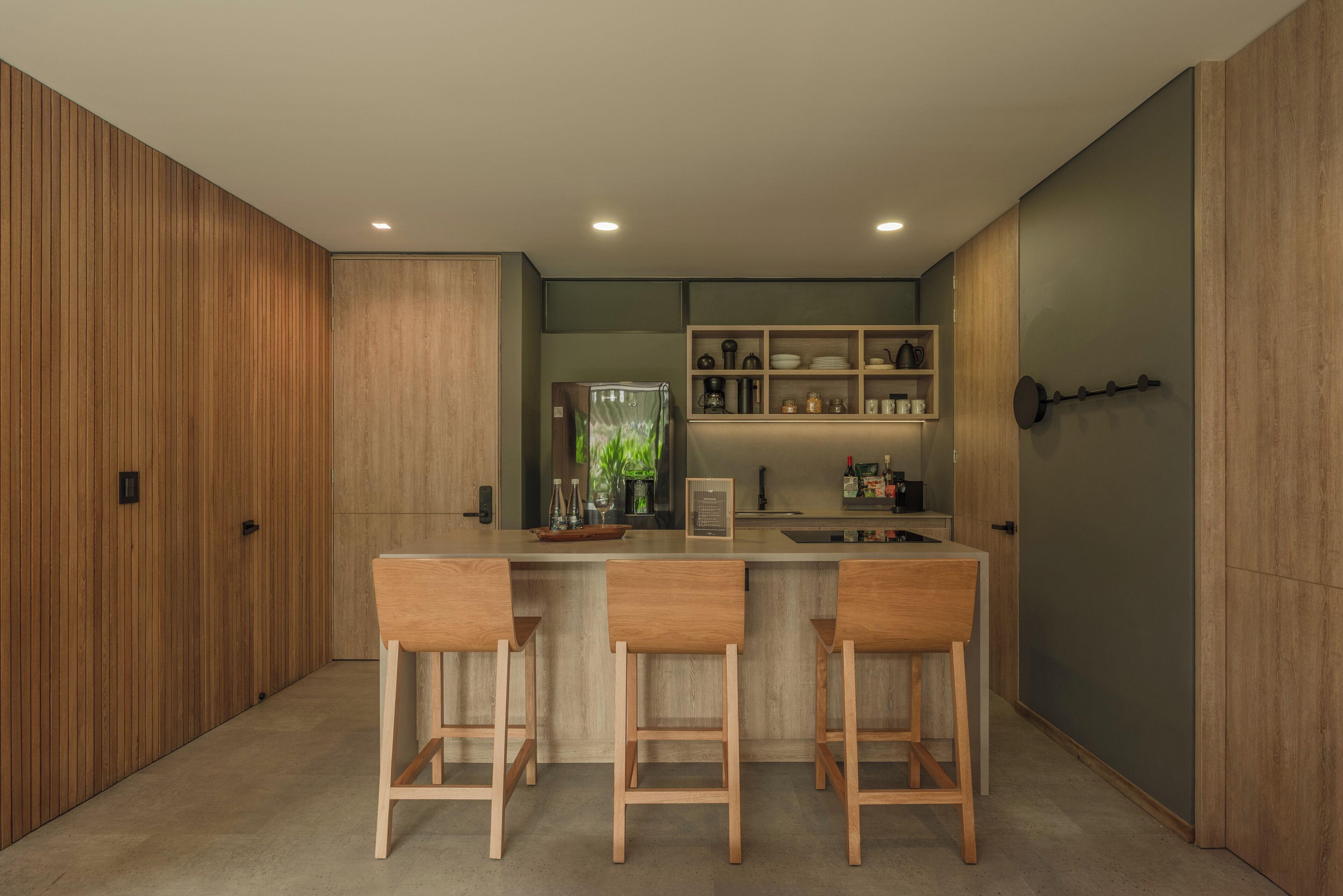 A modern kitchen with wooden paneling, a central island with bar stools, and built-in shelves with kitchenware.