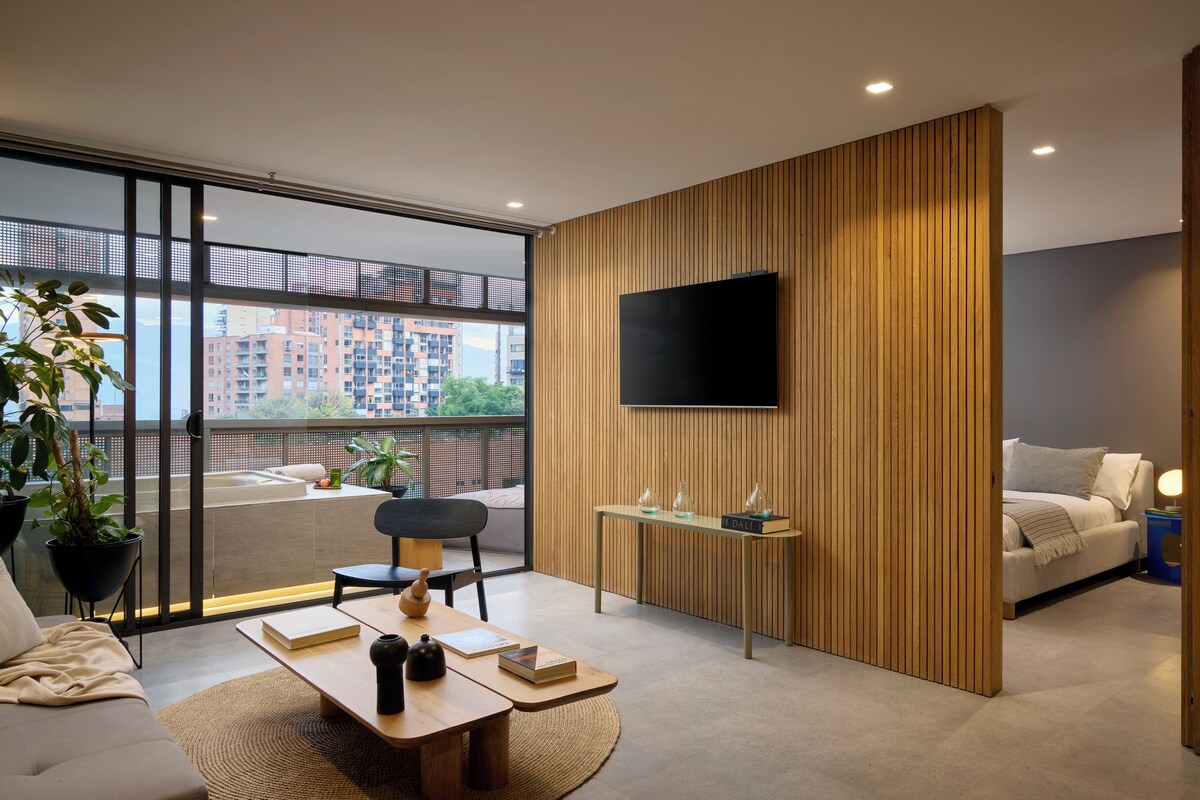 A modern living room with a large window, a flat-screen TV, a wooden accent wall, a sofa, a coffee table, and a small side table.