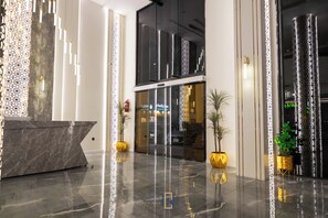 A modern lobby with a marble reception desk, glass doors, and potted plants. - Golden New Quraish (Jeddah)