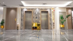 Un área de ascensores moderna con piso brillante, dos ascensores y un panel decorativo en la pared.