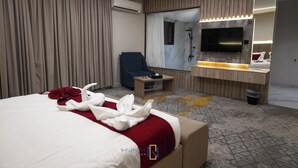 Habitación de hotel con una cama grande, un escritorio, una silla, un televisor, un espejo y un baño con ducha.