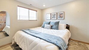 Een slaapkamer met een groot bed, een raam en drie kunstwerken in lijsten aan de muur.