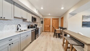 Een moderne keuken met witte kasten, een magnetron en een koffieapparaat. Er staat een houten eettafel met stoelen en een bankje.