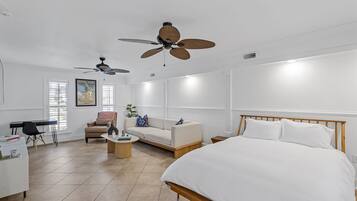 A modern bedroom with a large bed, a desk, a sofa, and two ceiling fans.