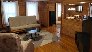 A cozy cabin interior with a sofa, a dining table with chairs, a small kitchen area, and a wooden floor. - Sleeps 10, close to shopping centers on quiet dead end street. (Brunswick)