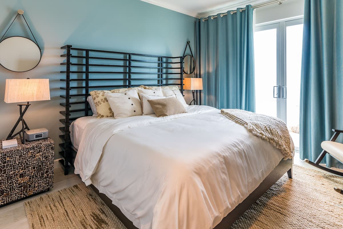 A bedroom with a bed, bedside lamps, a nightstand, and a window with curtains.