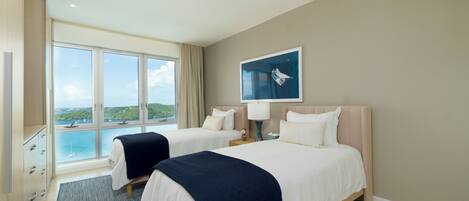 A hotel room with two beds, a large window with a view of the sea, and a painting on the wall.
