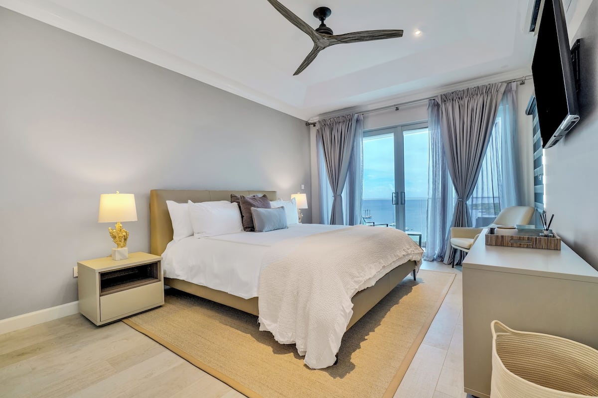 A modern bedroom with a large bed, bedside tables, a desk, and a ceiling fan.