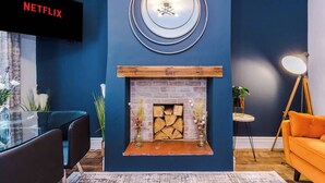 Uma sala de estar moderna com parede azul de destaque, lareira, TV na parede e espelho redondo.