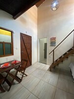 Uma sala de jantar com uma mesa de madeira posta para dois, uma porta de madeira e uma escada com corrimão.