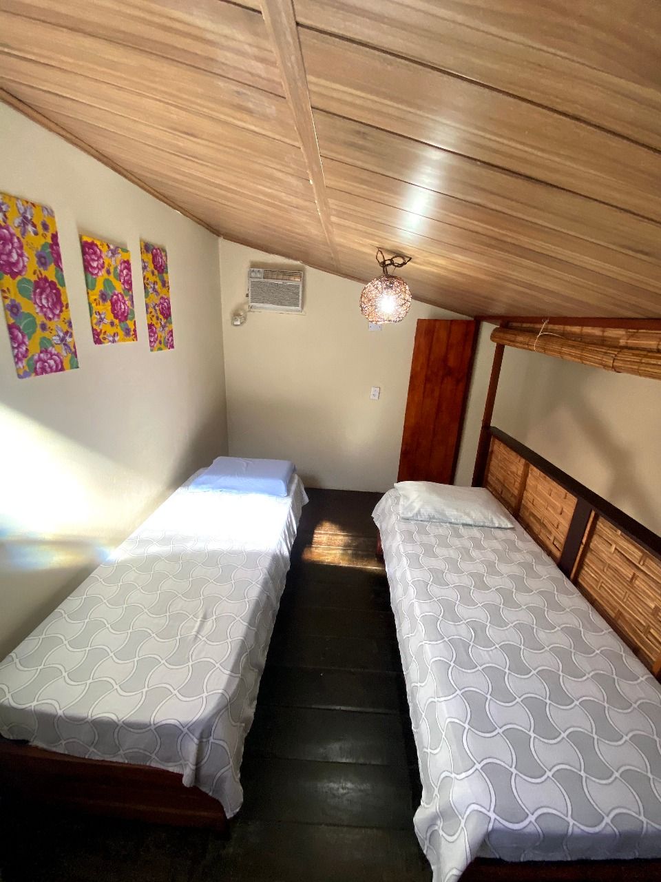 Une petite pièce avec deux lits, un plafond en bois et un climatiseur fixé au mur.