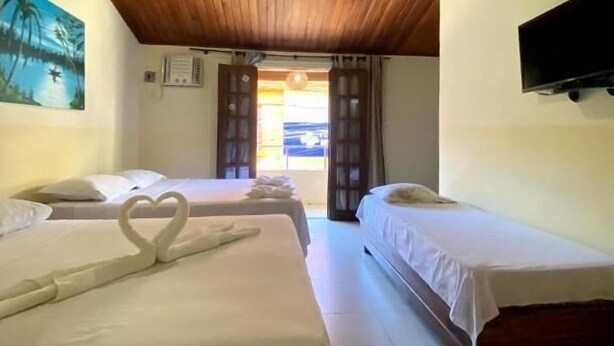 A hotel room with two beds, a wooden ceiling, a TV mounted on the wall, and a painting on the wall.