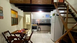 A dining area with a wooden table and chairs, a kitchen with a refrigerator and stove, and a wooden staircase.