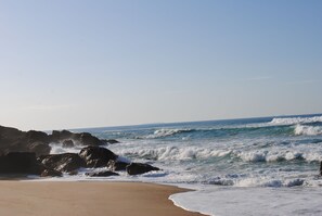 Une plage où les vagues se brisent sur le rivage, avec des rochers dans l’eau et un ciel dégagé.