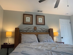 A bedroom with a bed, two bedside lamps, a ceiling fan, and two framed pictures on the wall.