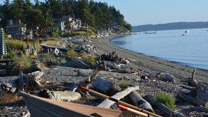 Une plage avec des bateaux et du bois flotté, des maisons en arrière-plan et un ciel dégagé.