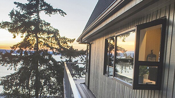Une terrasse en bois menant à une maison d’où l’on peut admirer un arbre et une étendue d’eau.