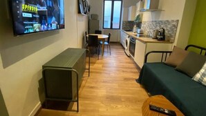 Un espacio habitable compacto con televisor montado en la pared, una pequeña zona de comedor, kitchenette y sofá.