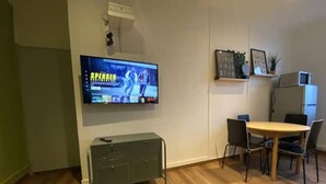 Una sala moderna con un televisor de pantalla plana montado en la pared, un mueble bajo, una mesa de comedor con sillas y un refrigerador.