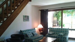 A living room with a sofa, a coffee table, and a lamp. There is a staircase on the left and a window with curtains on the right. - Gite with large swimming pool, play area, green space.  (Saint-Marcory)
