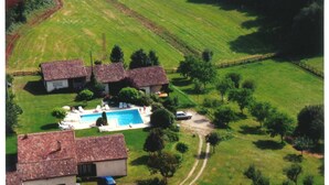 An aerial view of a property with two buildings, a swimming pool, and surrounding green fields. - Gite with large swimming pool, play area, green space.  (Saint-Marcory)
