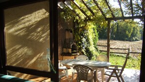A patio with a table and chairs, a grill, and a view of a garden and field. - Gite with large swimming pool, play area, green space.  (Saint-Marcory)