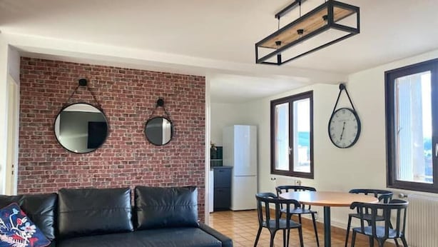 Ein Wohnzimmer mit Backsteinwand, einer schwarzen Ledersofa, einem Holztisch und einem Essbereich mit Tisch und Stühlen.