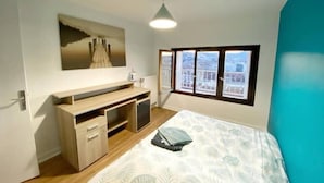 Ein Schlafzimmer mit einem Bett, einem Schreibtisch, einem Stuhl, einem Fenster mit Stadtblick und einer Deckenleuchte.