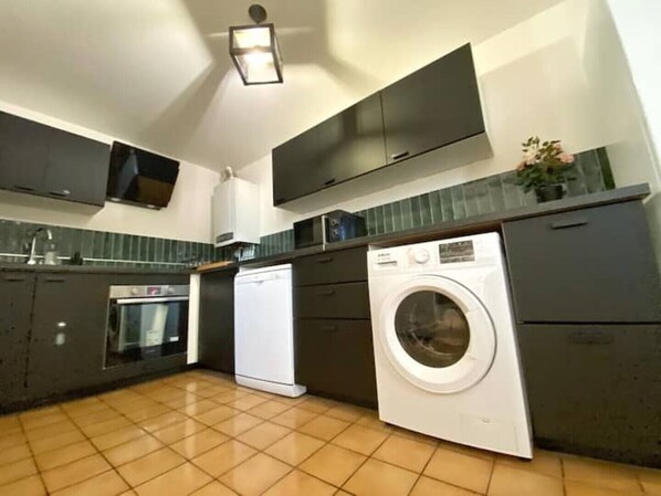 A compact kitchen with a built-in oven, a washing machine, and a microwave.